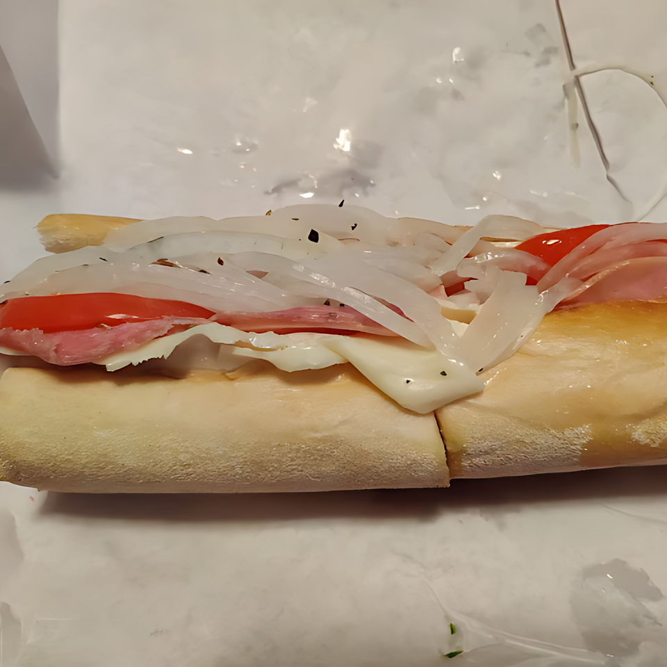 A close-up of a submarine sandwich filled with sliced meats, cheese, tomatoes, and onions.