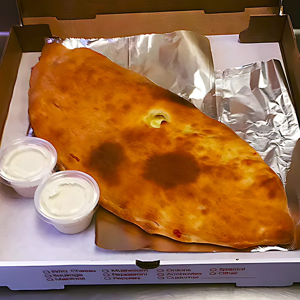 A golden-brown calzone in a pizza box with two small cups of dipping sauce.
